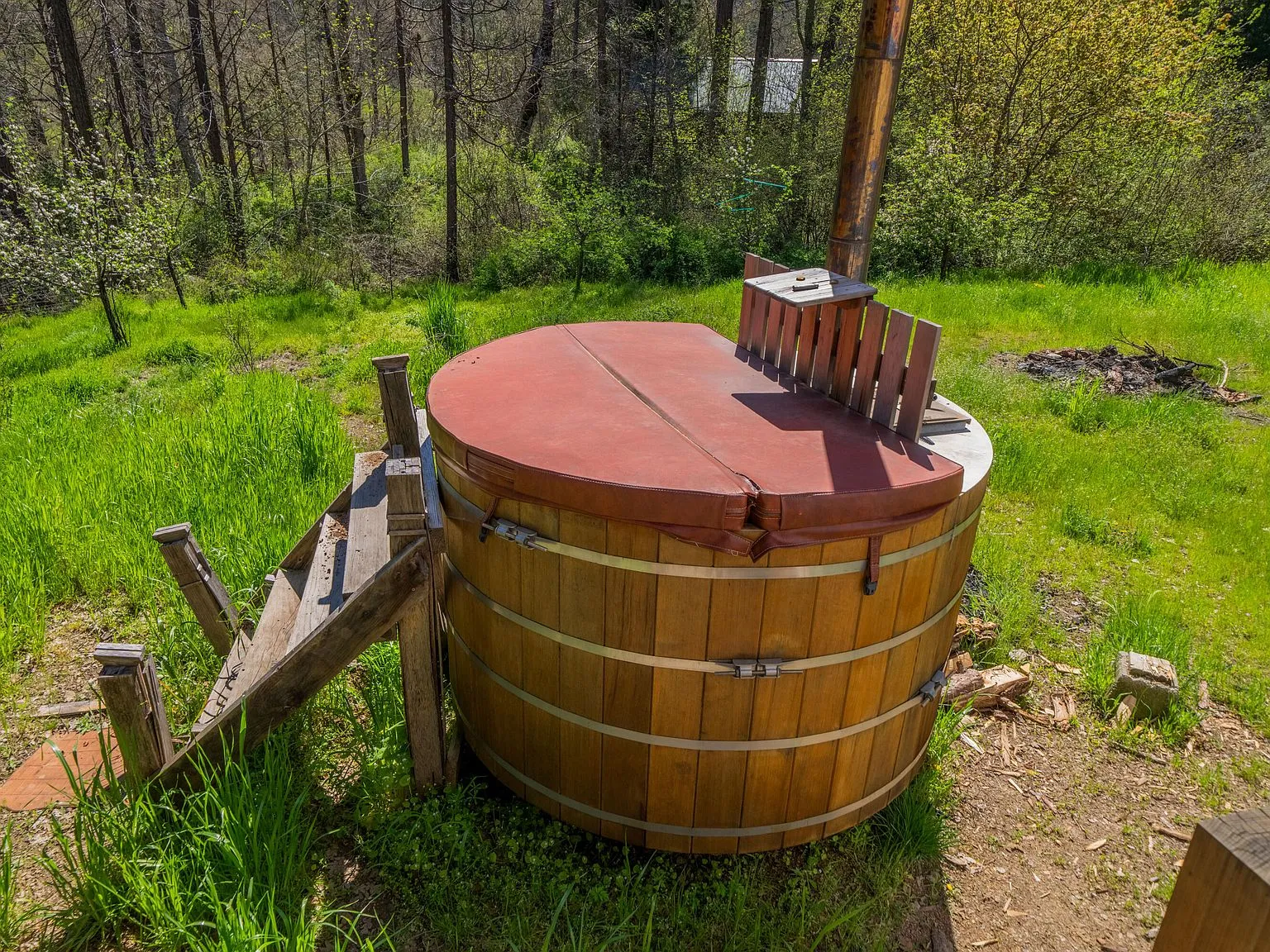 The wood-fired hot tub set in the yard, with the house visible behind it