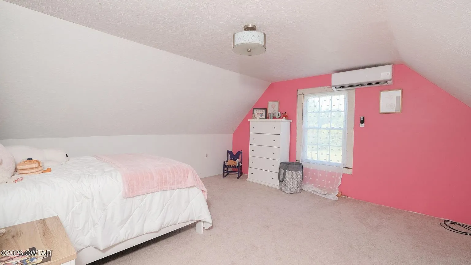 An upstairs bedroom with a pink wall, a bed under the slope and a mini-split head