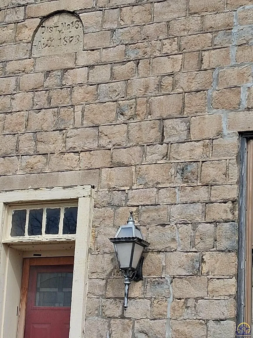 The stone wall with the date stone above and a lantern by the door