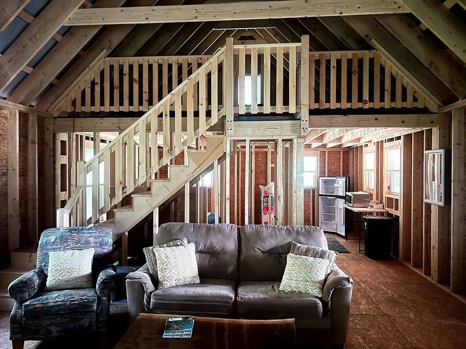 Inside the cabin: the open stud walls, the stair to the loft and a sofa on the subfloor
