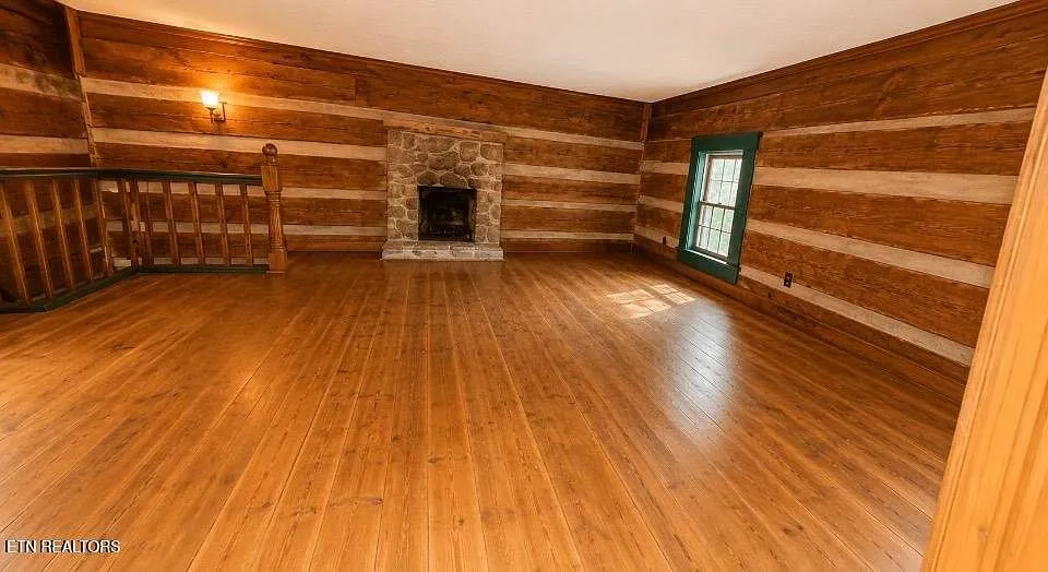 A log room with a smaller stone fireplace and a railed stairwell opening