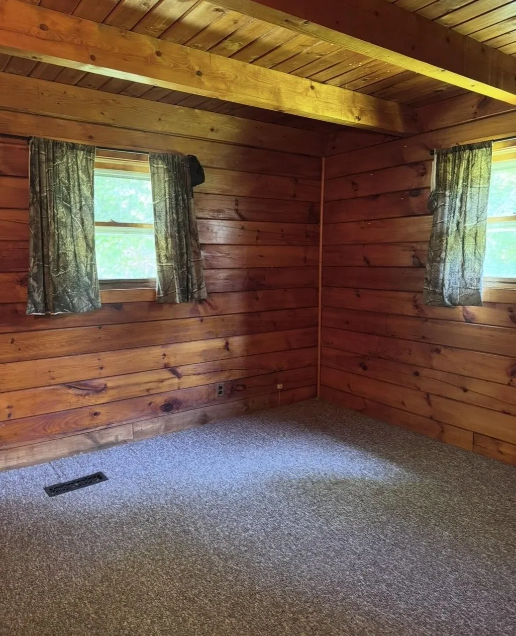 A bedroom with the log walls, the two windows and the carpet