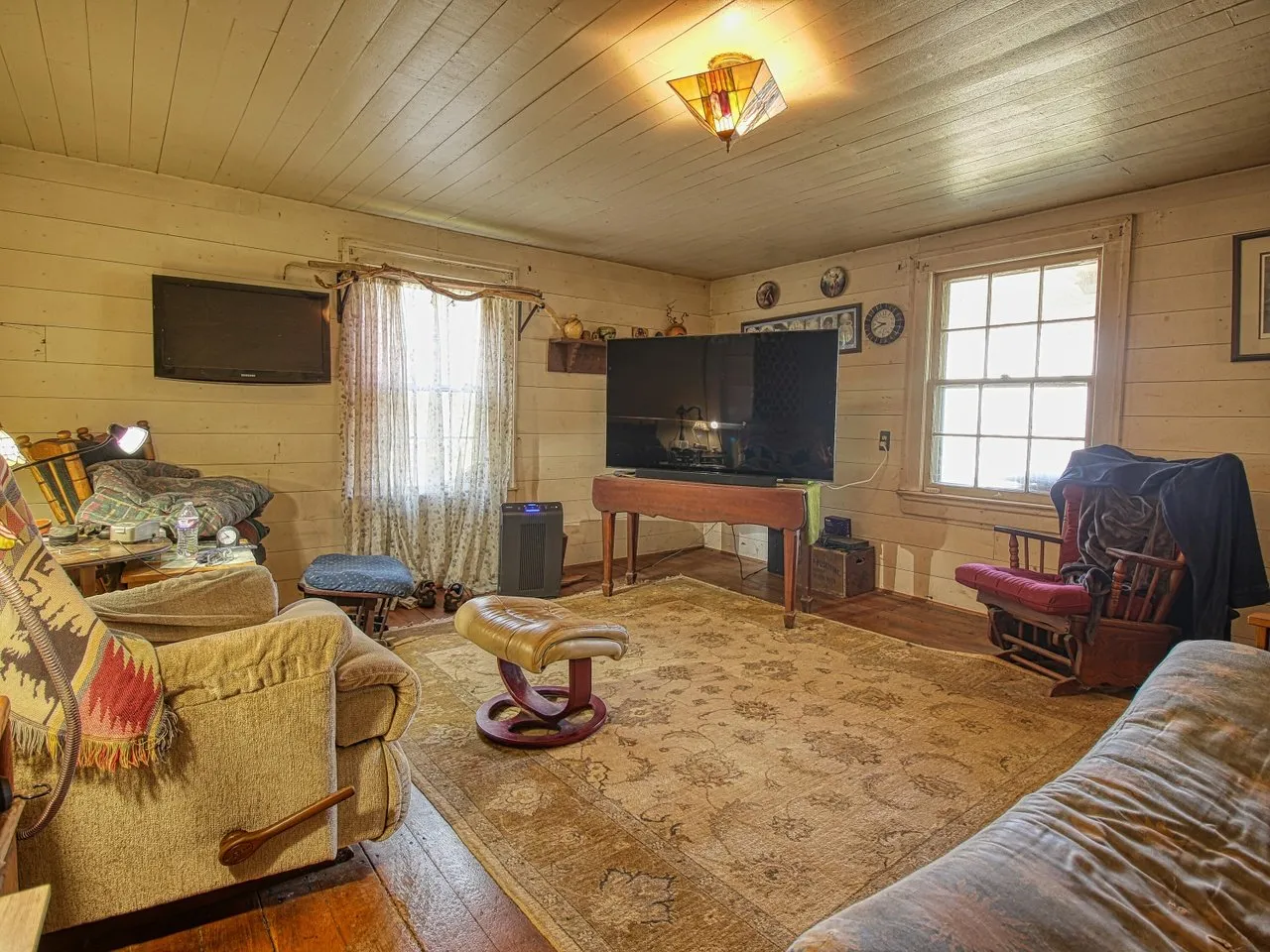 The living room with a sofa, a television on the wall and two windows