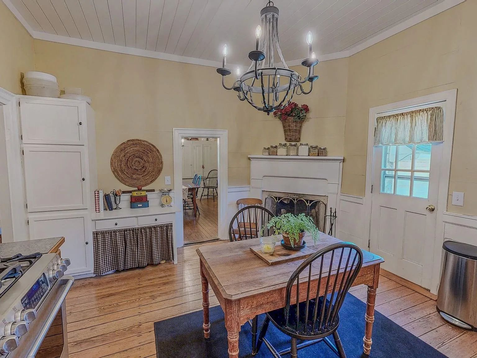 A yellow-walled sitting room with a fireplace mantel and a pie safe