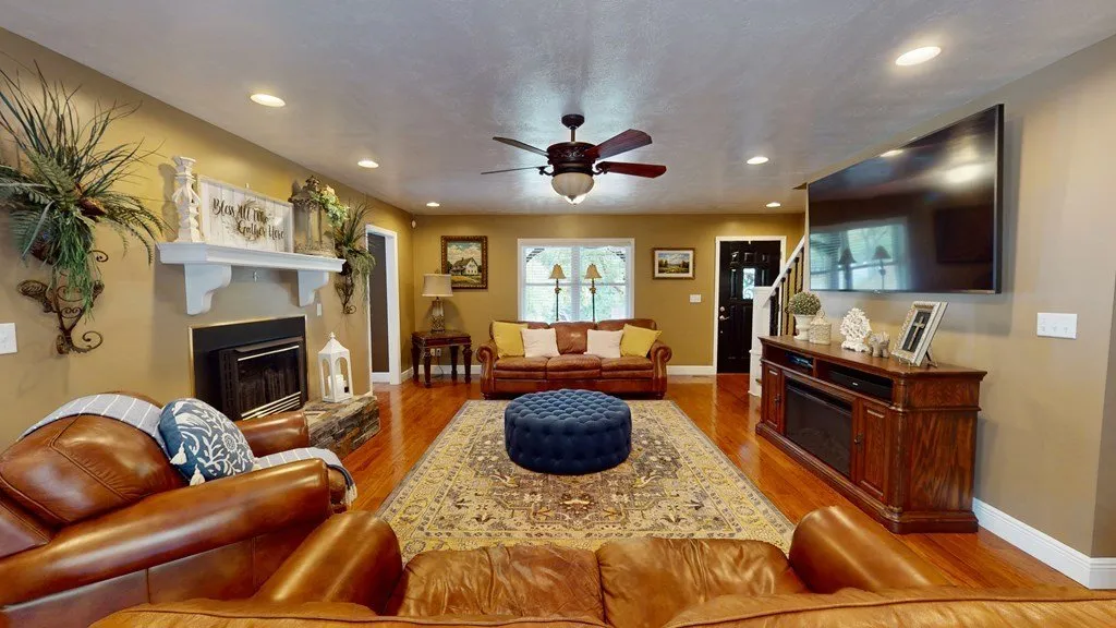 The living room with a stone fireplace, leather sofa and a ceiling fan