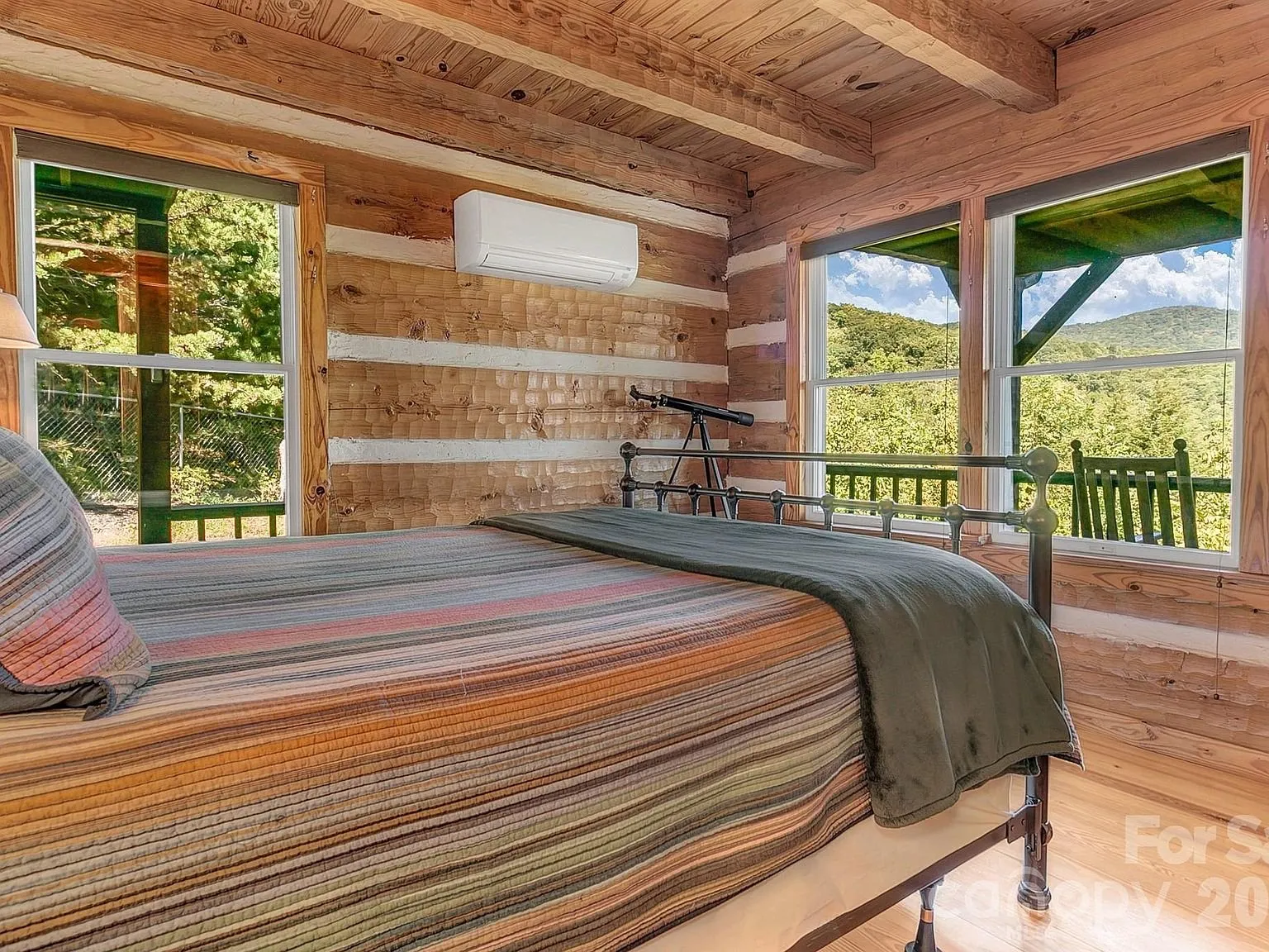 A bedroom with a dark metal bed frame and striped bedding, log walls on three sides