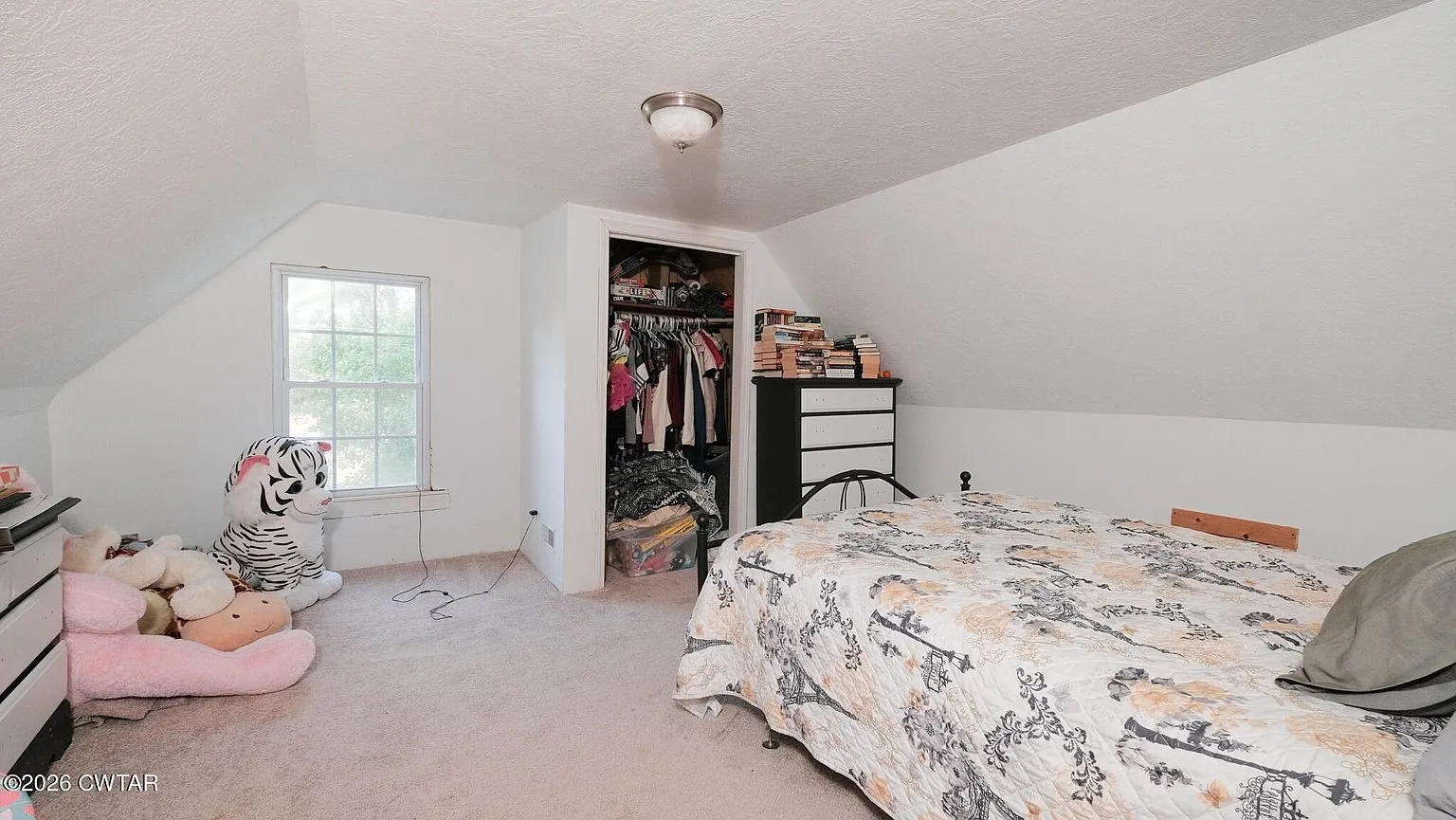 An upstairs bedroom with a bed and a closet in the knee wall