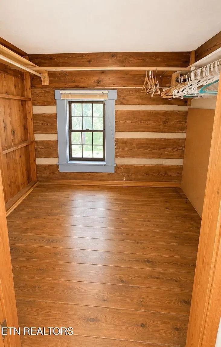 A log-walled room with a window and a closet rod