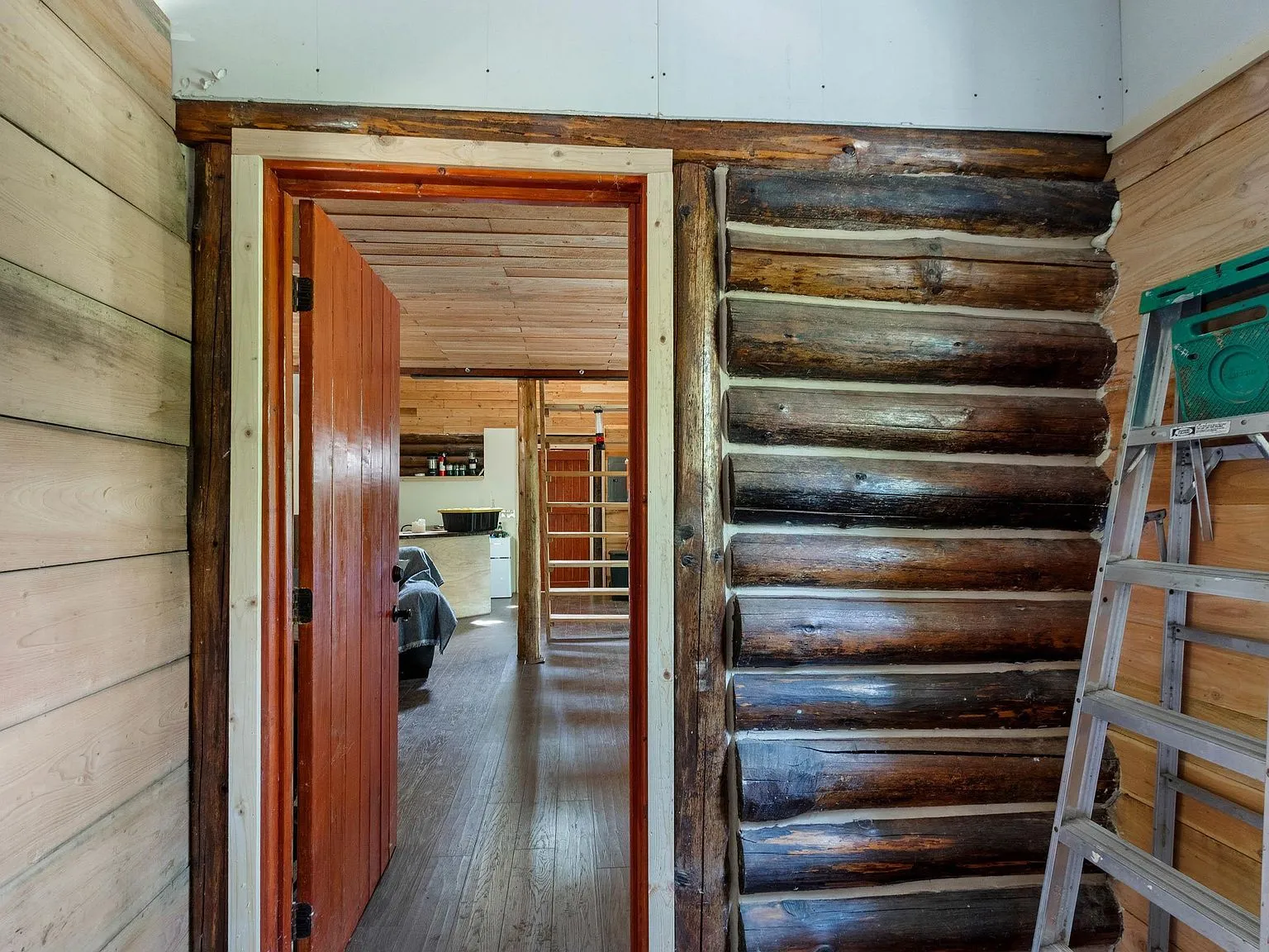 An unfinished room with a ladder, exterior door and stacked wood paneling, framed and ready to finish