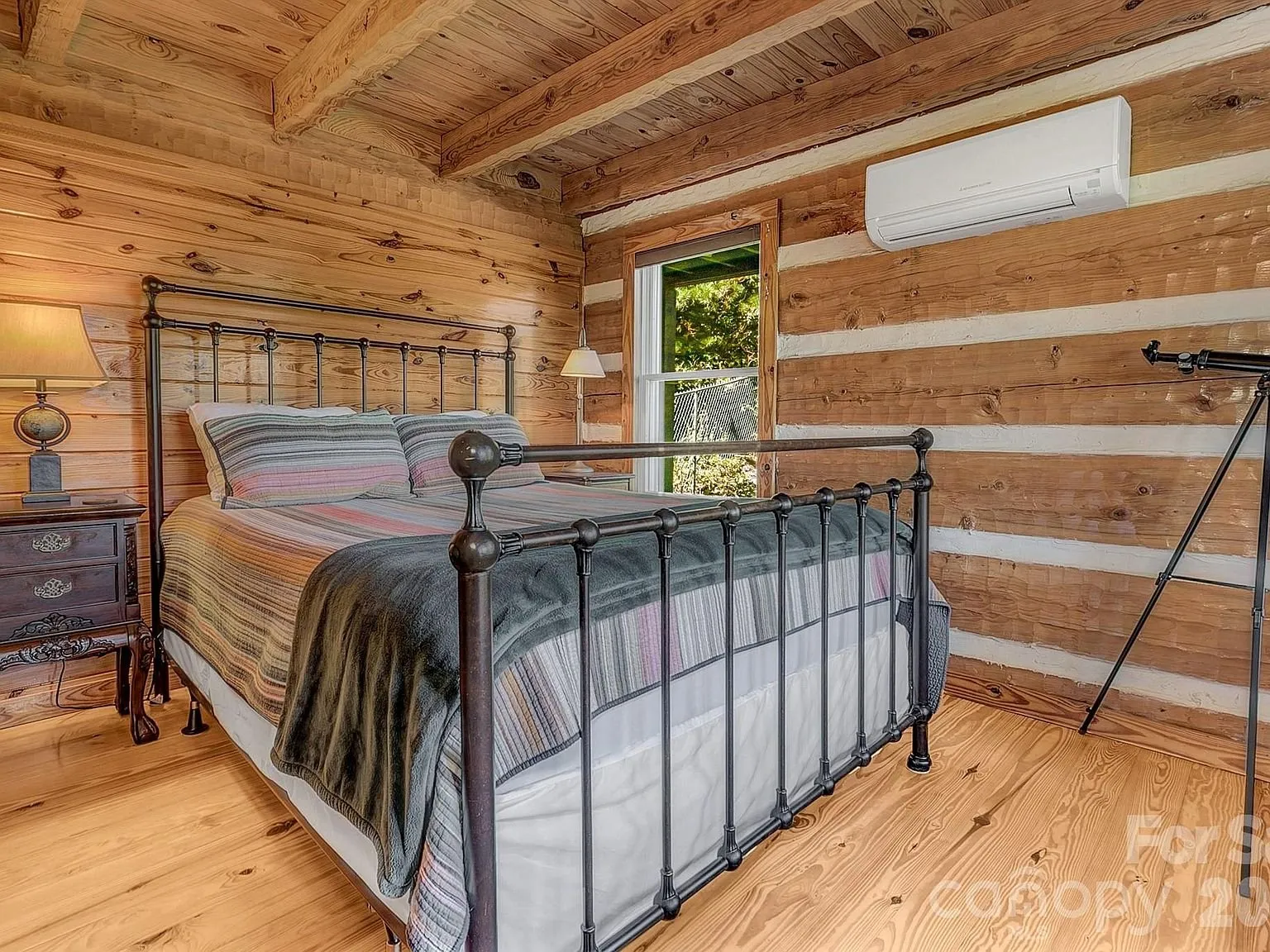 A bedroom with a metal bed frame and a nightstand against the log wall