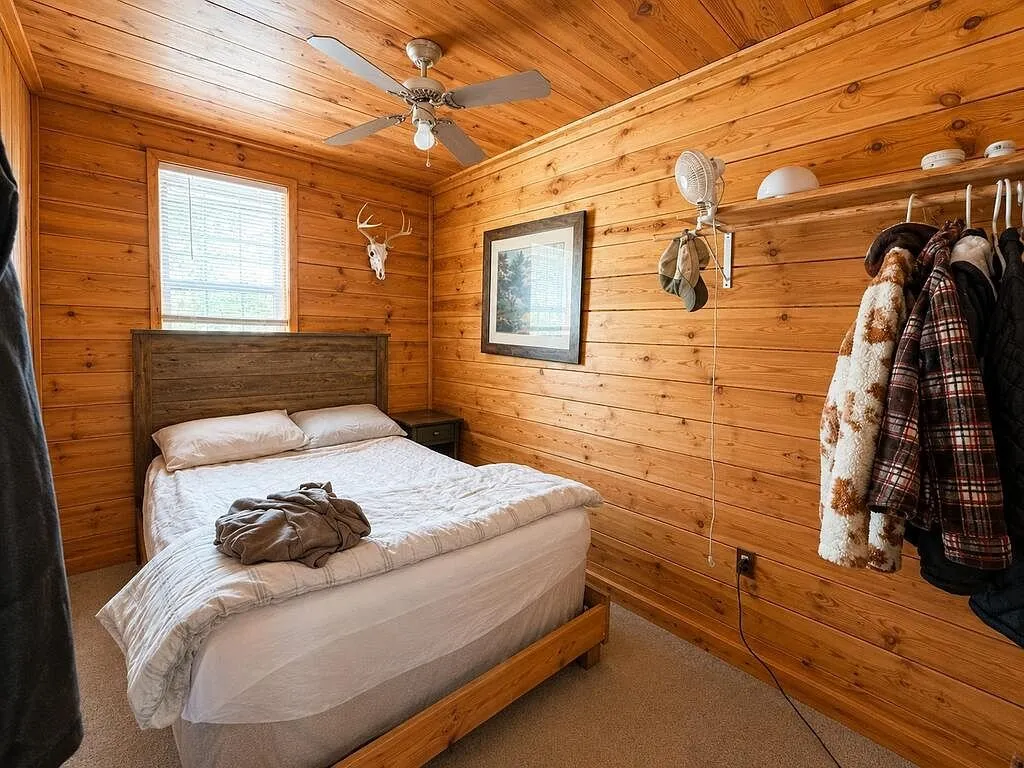A bedroom with a bed under the window and coats on the wall