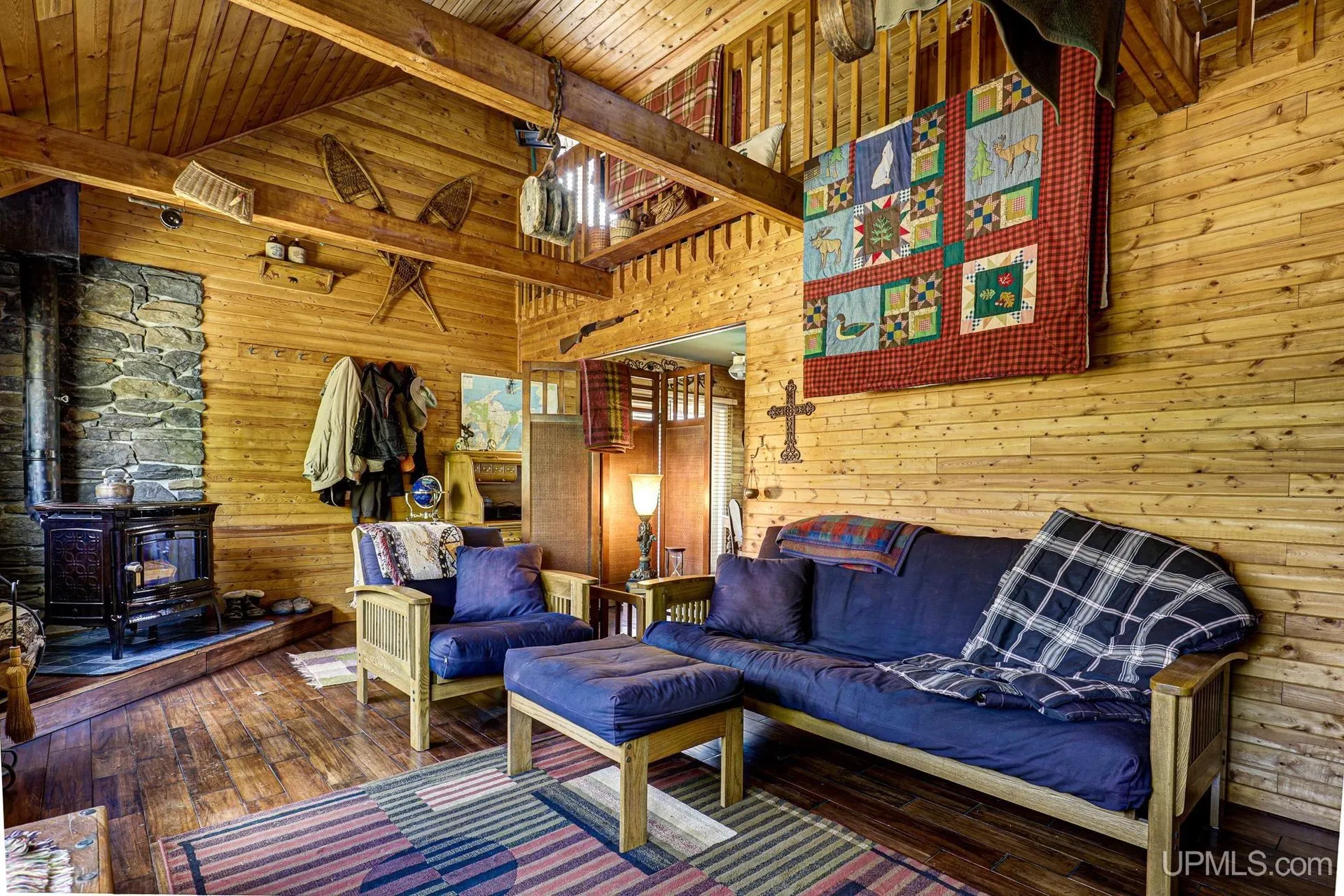 The living room with a futon, quilts on the wall and the stairs to the loft