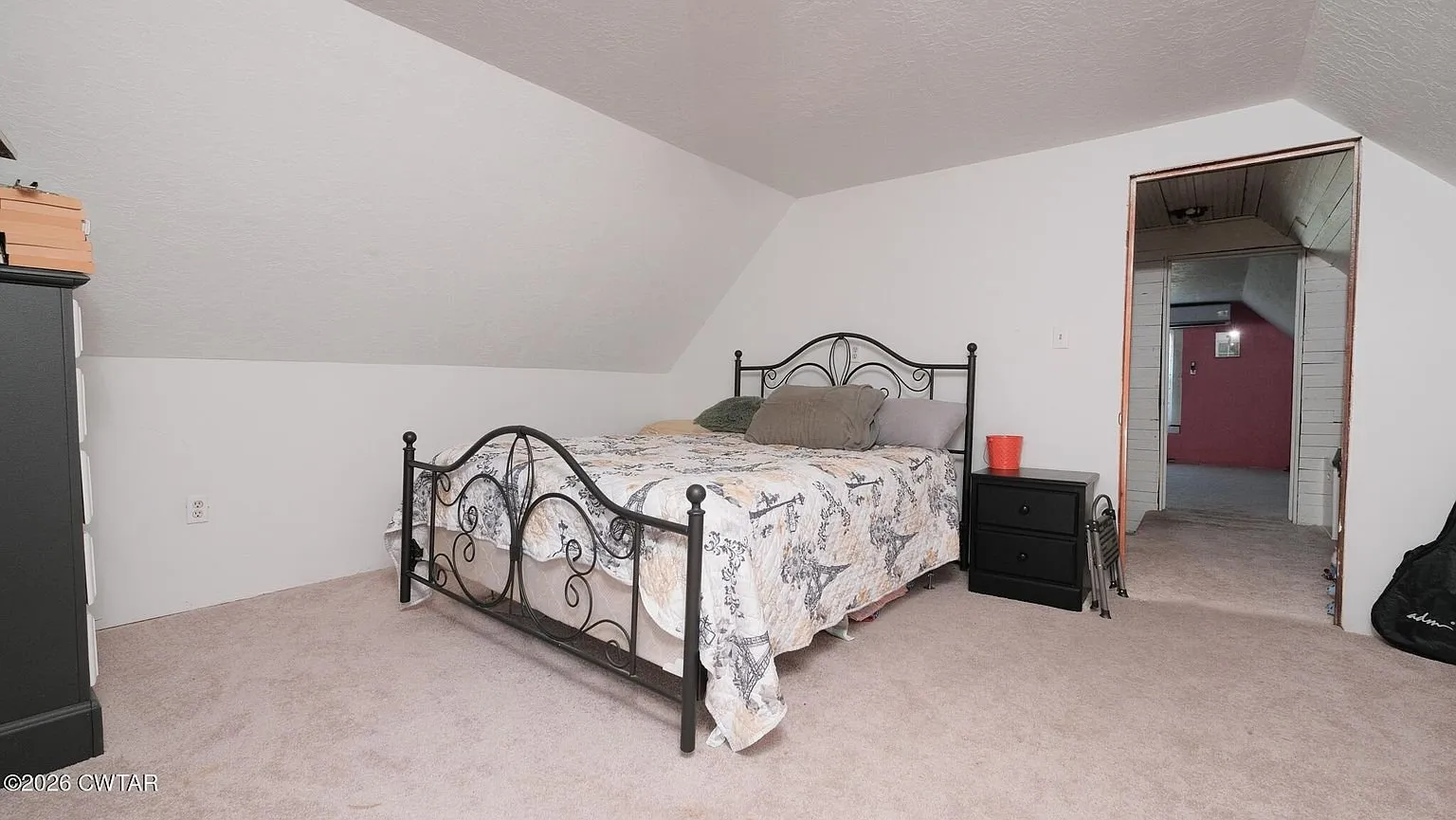 An upstairs bedroom with an iron bed and the door to the hall