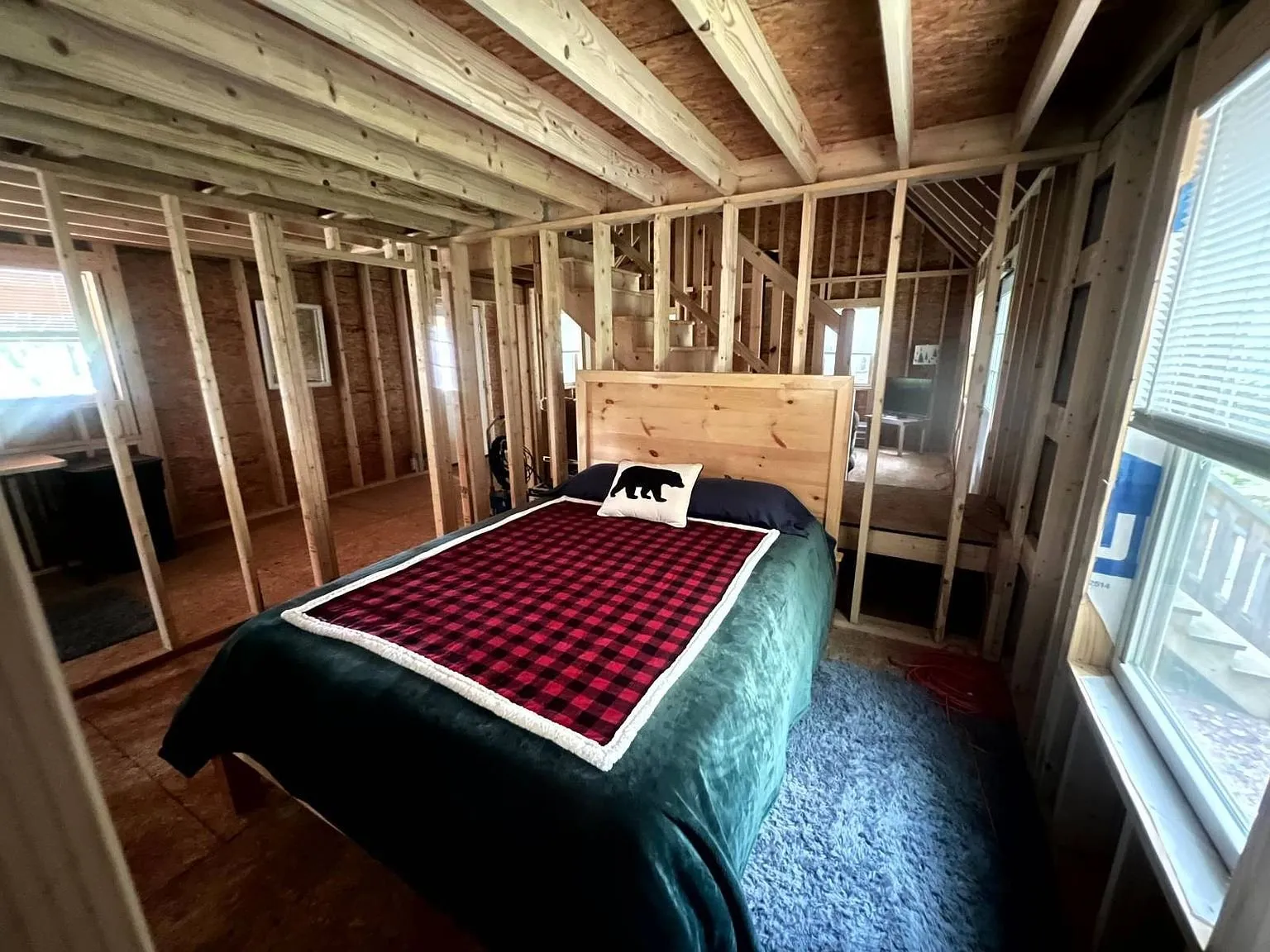 A bed set up against the open stud wall under the loft