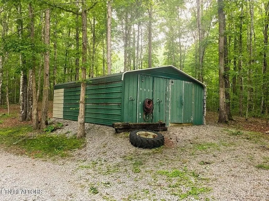 A green metal storage building set back in the trees on the property