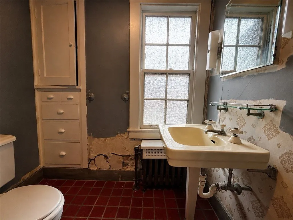 A bathroom with a pedestal sink, a radiator and cracked plaster