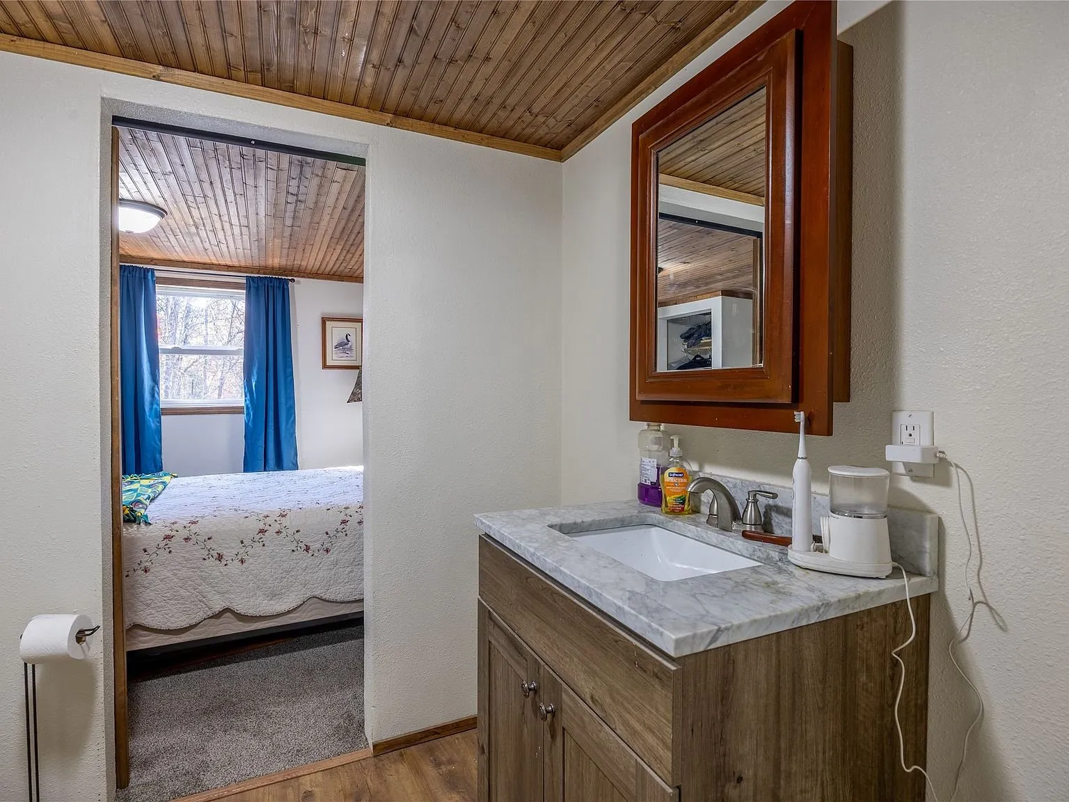 A bathroom vanity and mirror under a sloped wood ceiling
