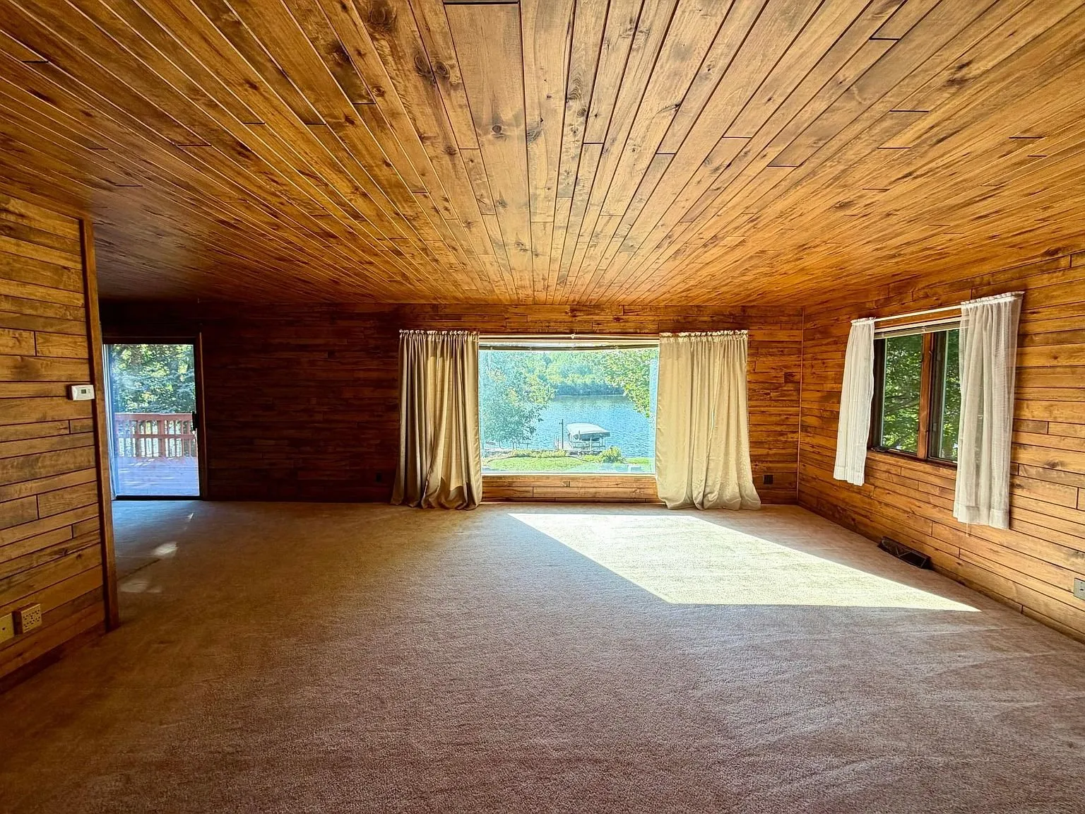 The living room with the wood ceiling and the wide window