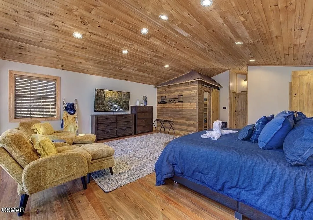 A bedroom with a blue bed, a chaise and a dresser under a sloped ceiling