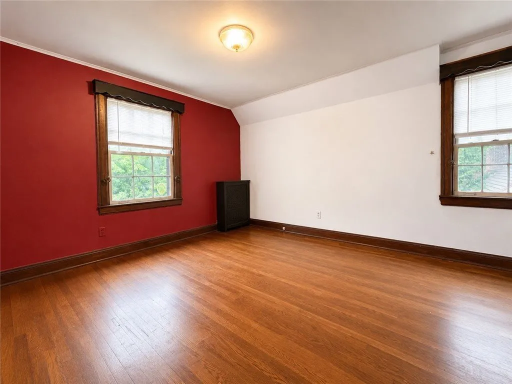 A bedroom with one red wall and hardwood floors