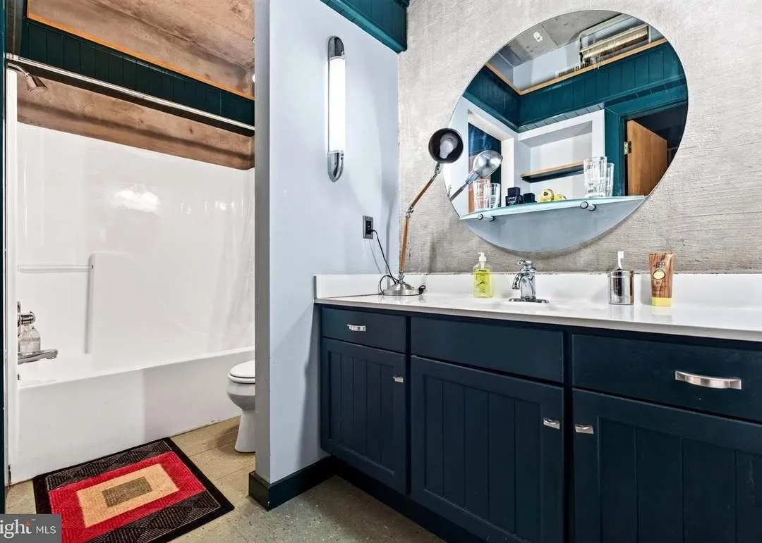The full bathroom with a navy vanity, round mirror and tub
