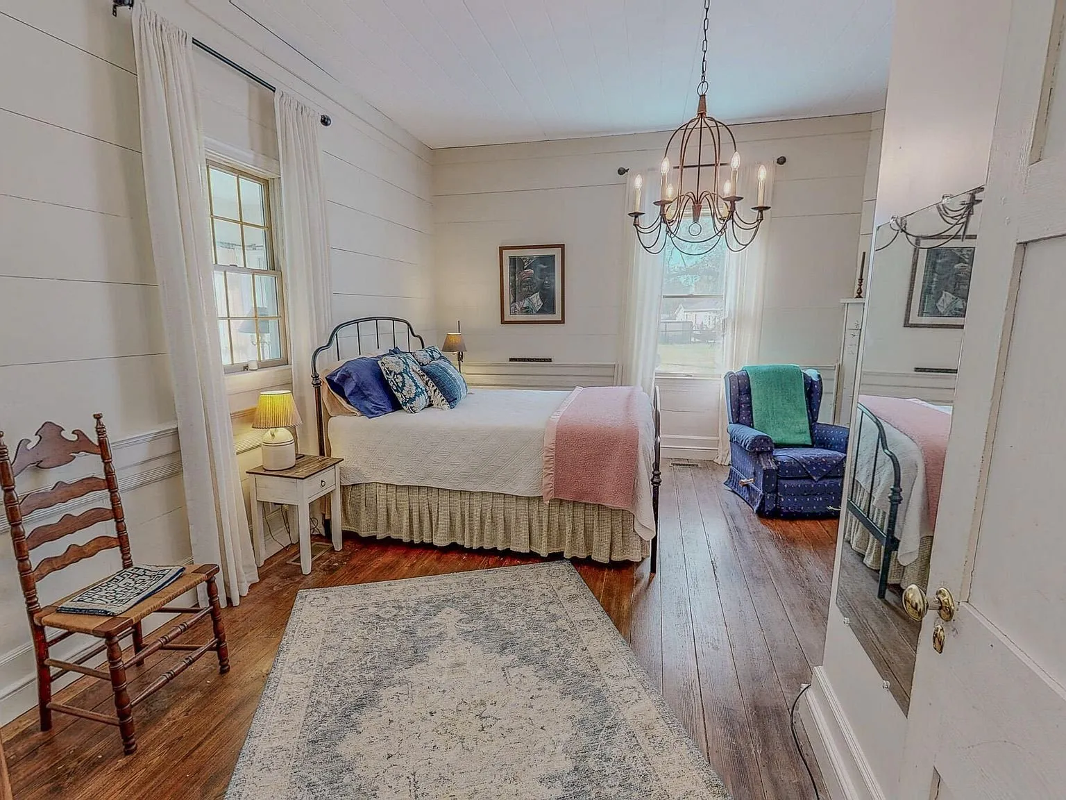 A bedroom with a four-poster bed and a mirrored dresser opposite