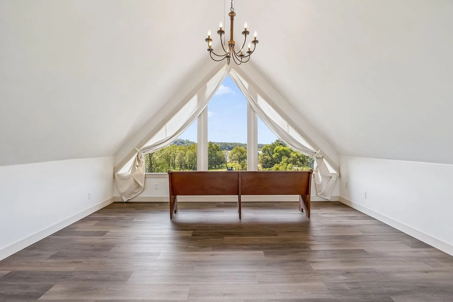 The upstairs room under the peak with the triangle window and a bench