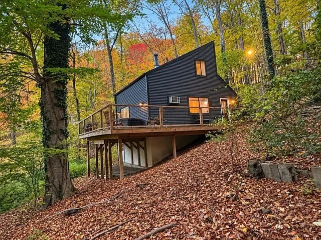 The cabin seen from below on its raised deck foundation, framed by fall foliage