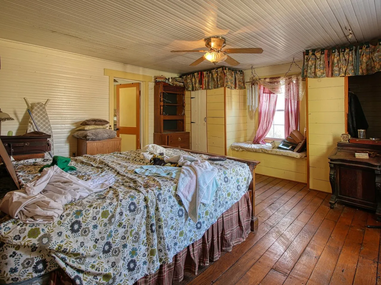 A bedroom with a quilt on the bed, wood floors and pink curtains