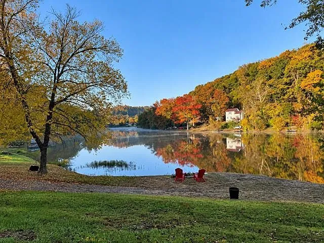 A view of Lake Chaweva's shoreline with Adirondack chairs and fall color reflected in the water