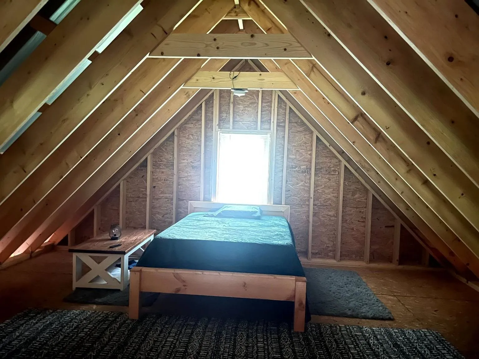 The loft under the rafters with a bed and a gable window