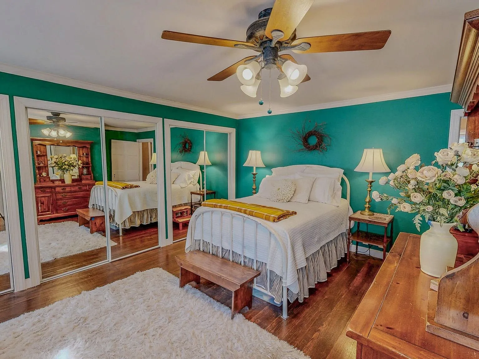 A teal-walled bedroom with mirrored closet doors and a white bedspread