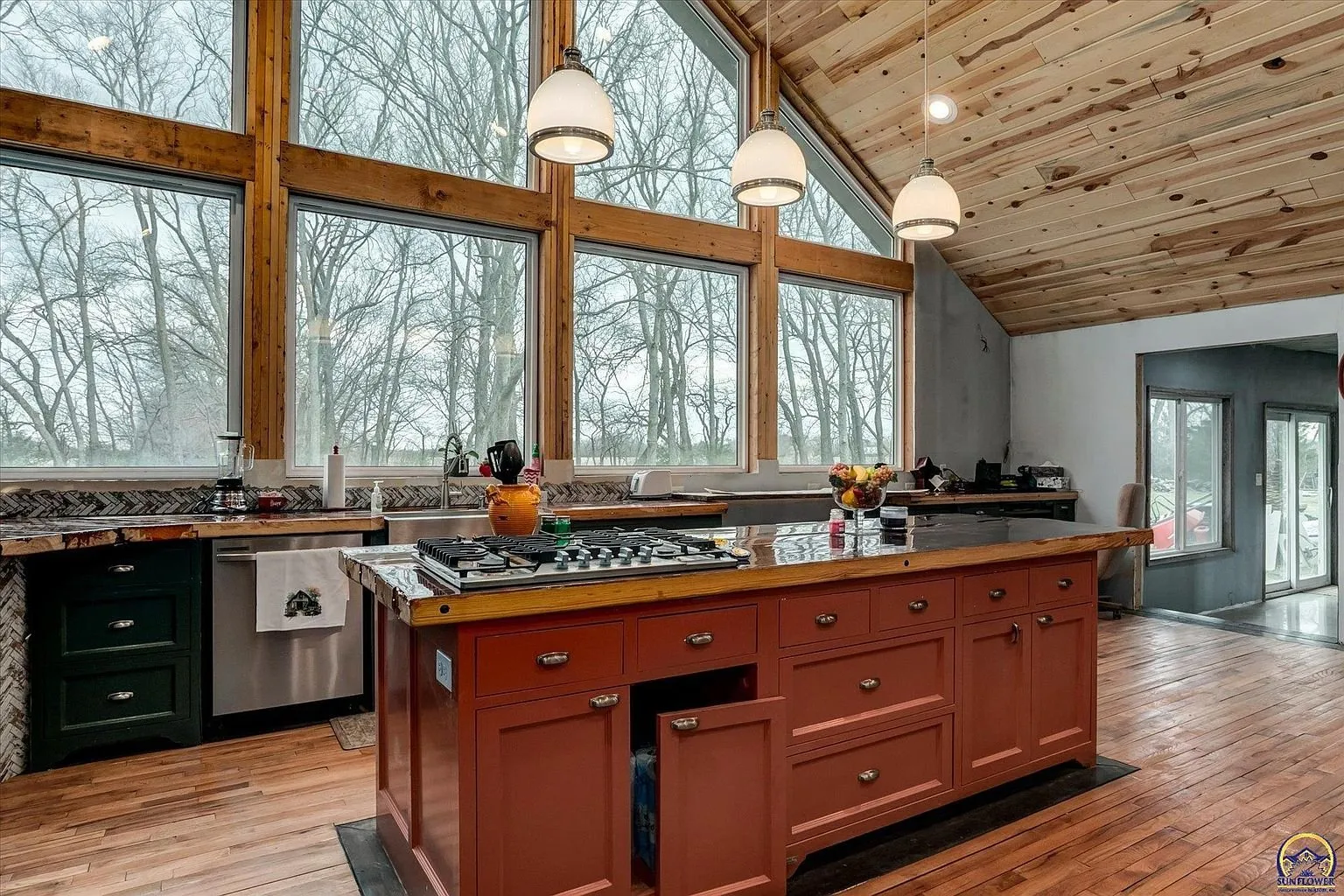 The kitchen with the island, the green cabinets and the wall of windows