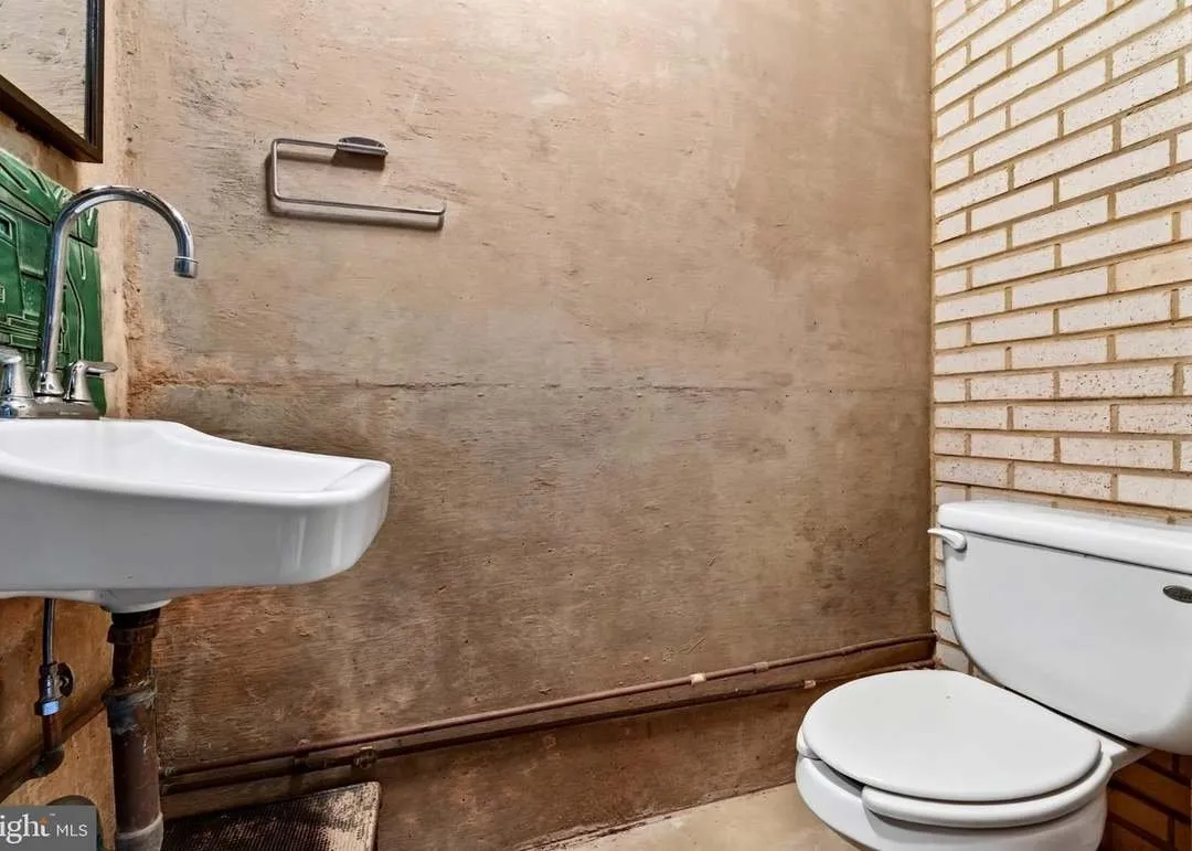 A half bathroom with exposed brick and a pedestal-style sink