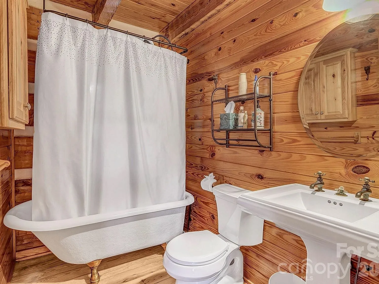 A bathroom with a clawfoot tub, pedestal sink and shower curtain
