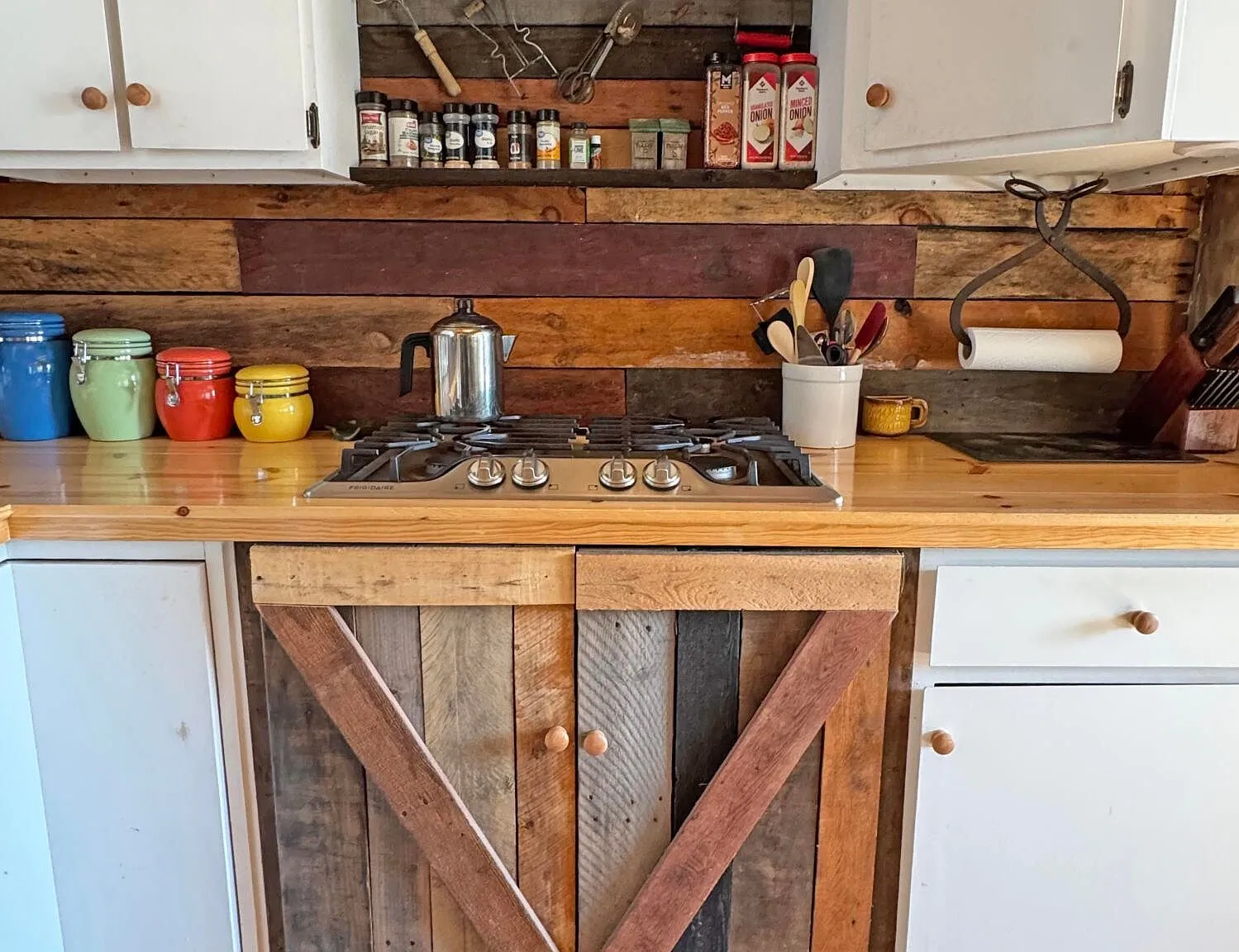 The cooktop set into the reclaimed wood counter, jars on the shelf above