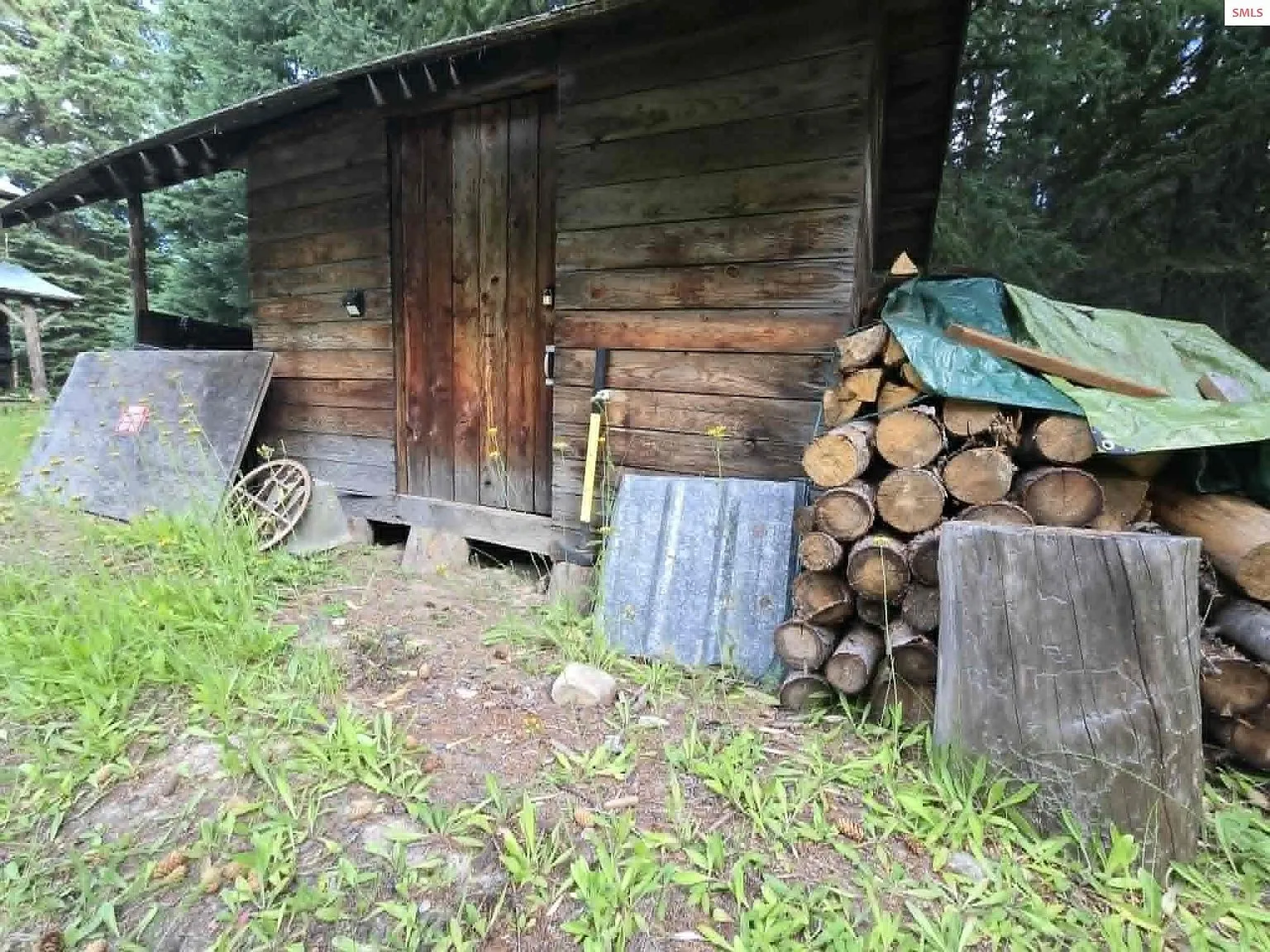 A storage shed with a sloped roof, firewood stacked and covered beside it