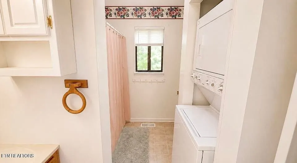 The laundry room with a curtained shower alcove and a stacked washer and dryer