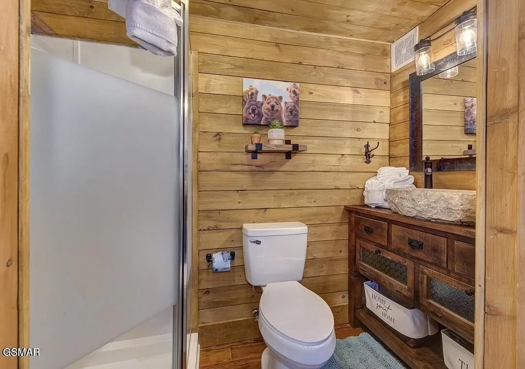 A bathroom with a glass shower, toilet and wood vanity