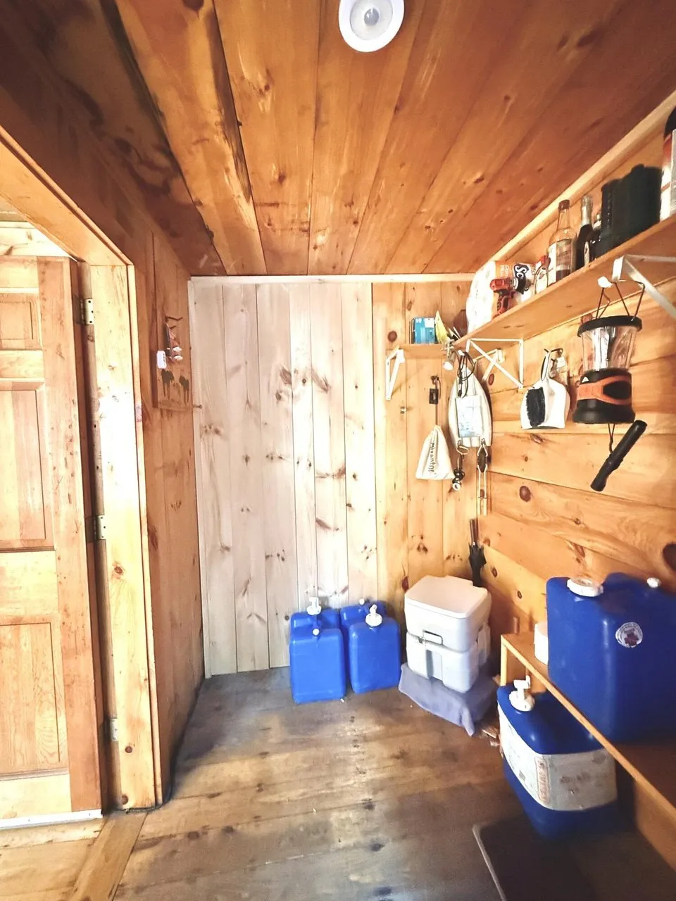 The entry with the blue water jugs, a portable toilet and lanterns on the shelf