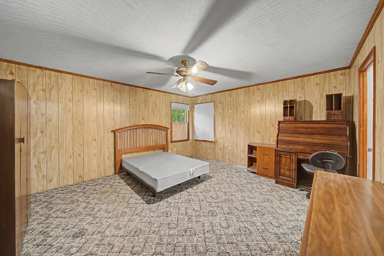 A bedroom with panelled walls, a bed frame and a desk