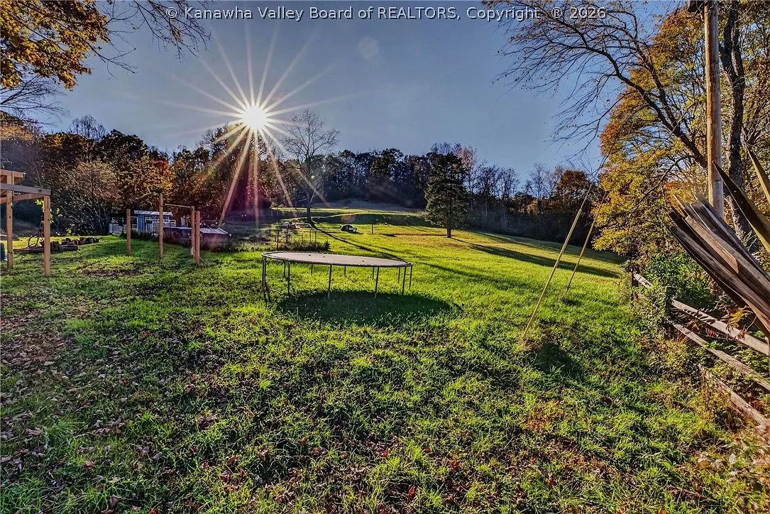 A wide view of the sloped 14-acre lot with a trampoline and tree line