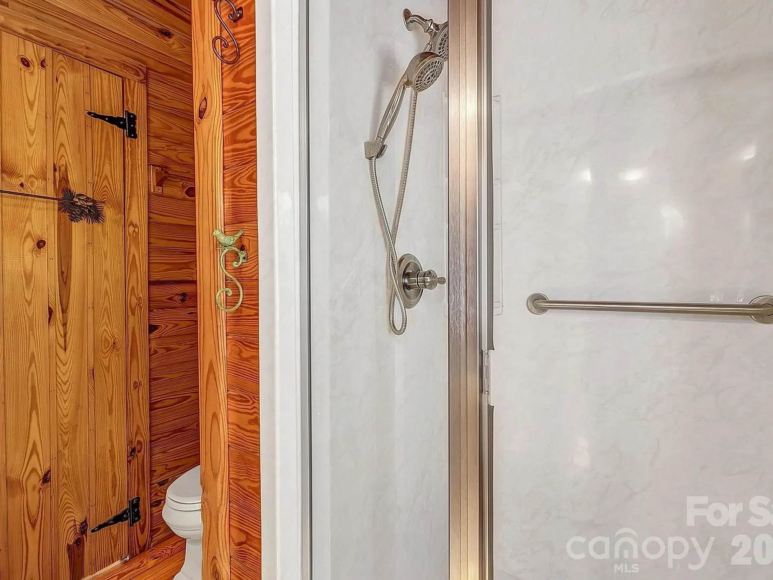 A walk-in shower with a handheld sprayer and grab bar
