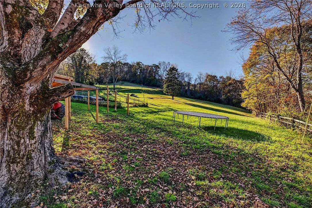 A second view of the open pasture with a trampoline and wood fencing