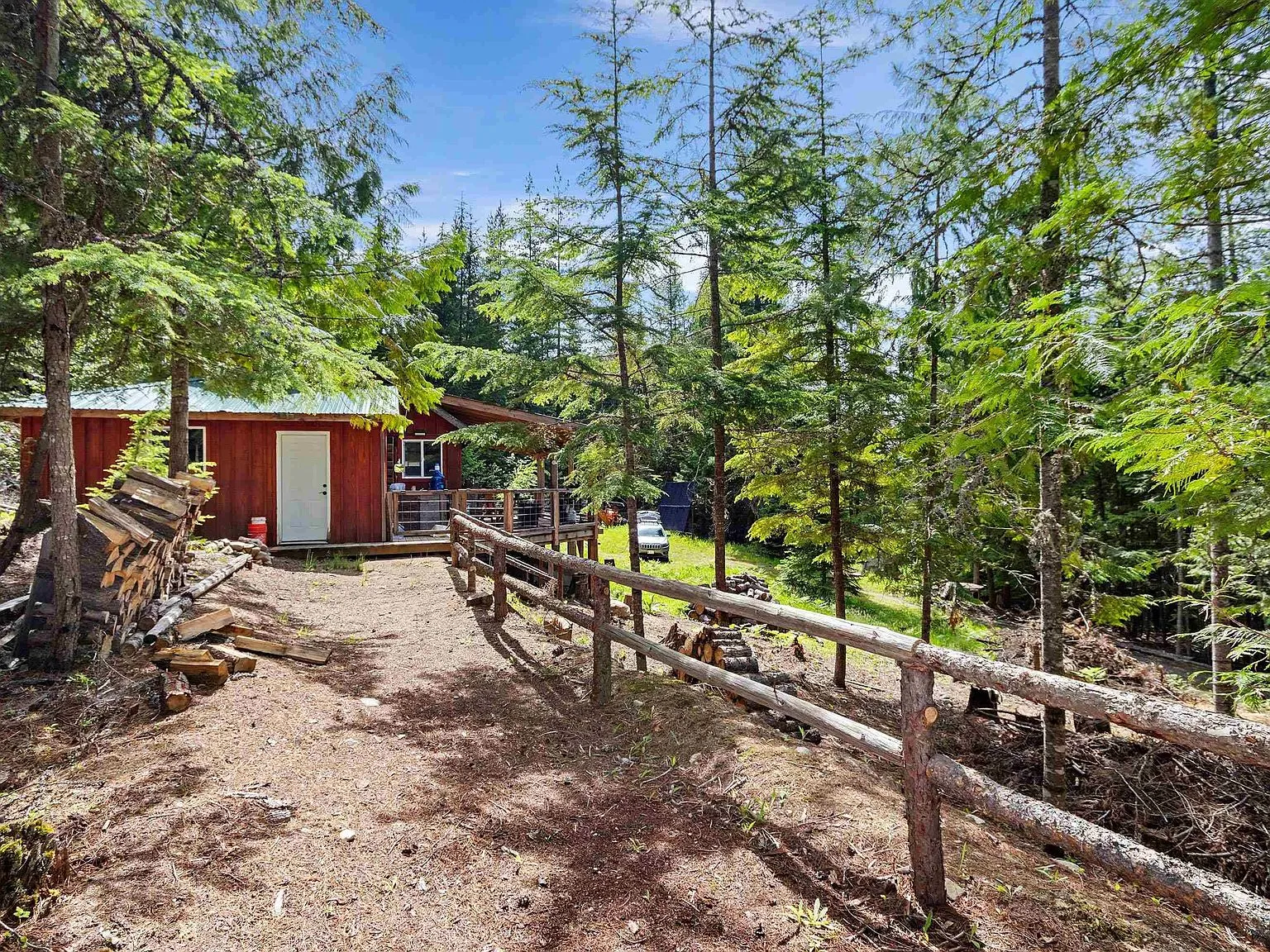 A wood storage building and the cabin's clearing, framed by pines and a split-rail fence