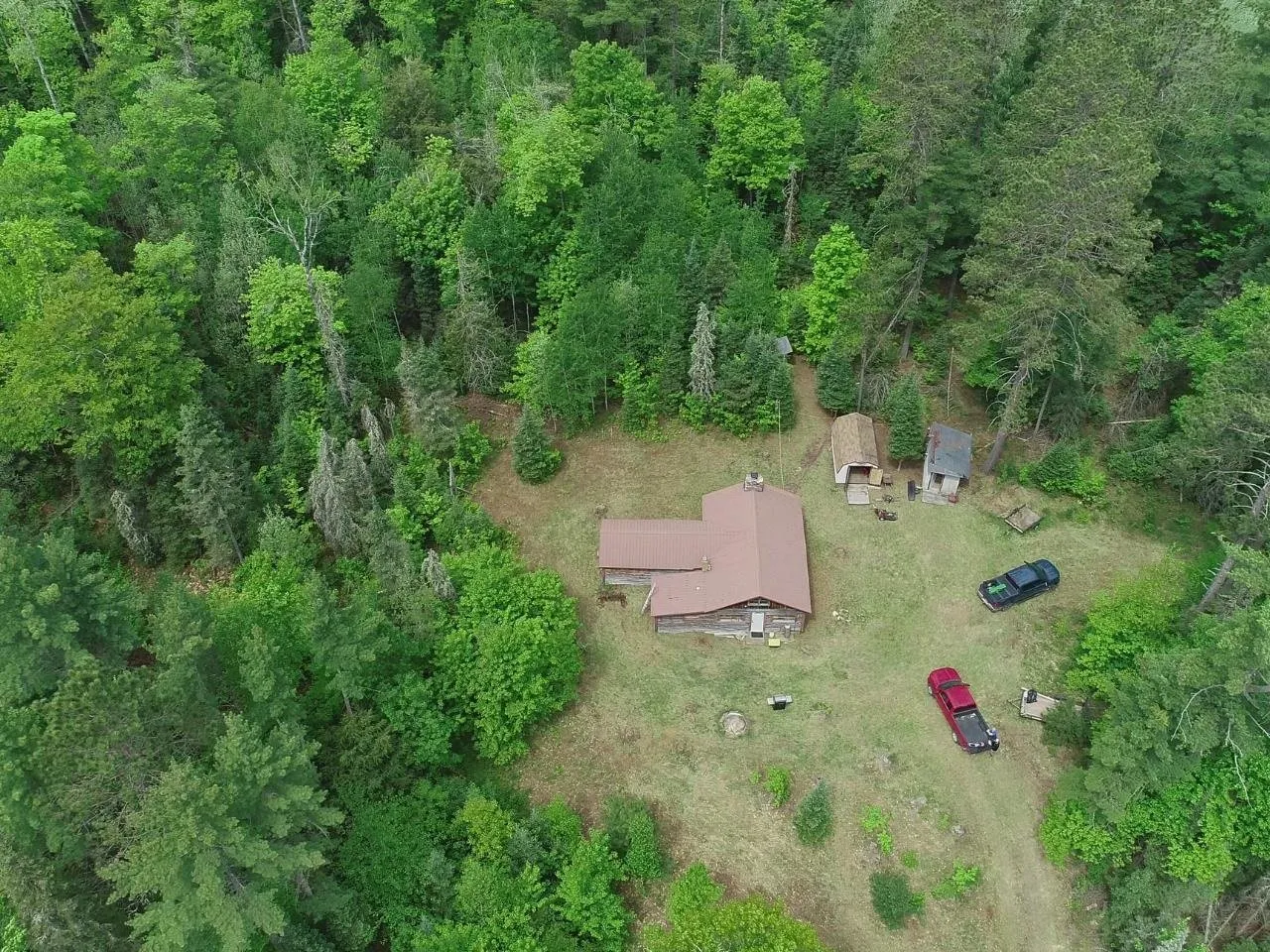 The clearing and the outbuildings from the air with vehicles parked by the camp