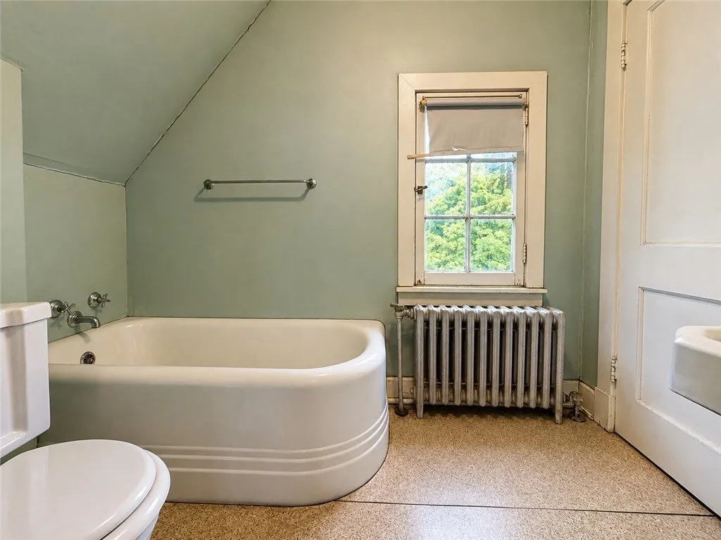 The third-floor bathroom with a tub, a radiator and a dormer window