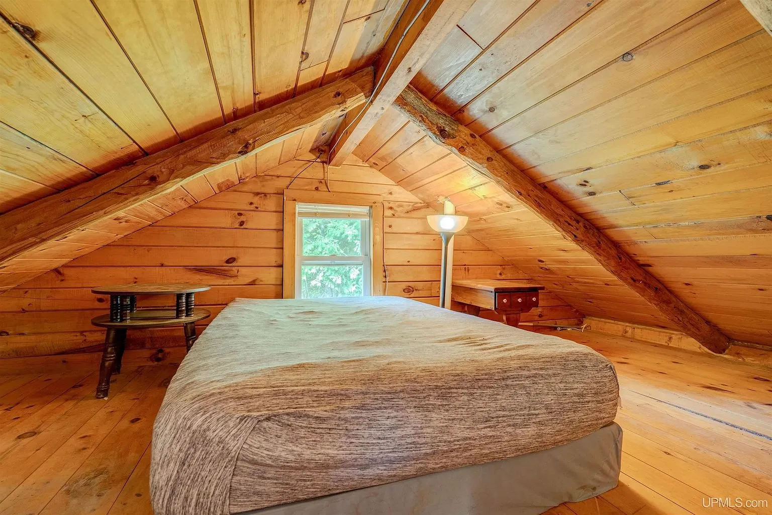 The loft with a bed under the sloped log ceiling