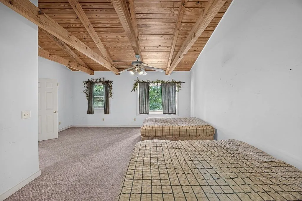 An upstairs bonus room with exposed beams and ceiling fan