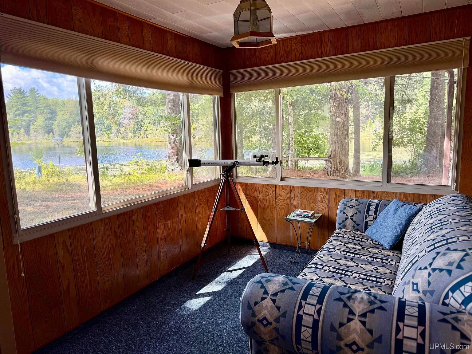 The three-season room with a sofa and a telescope facing the lake